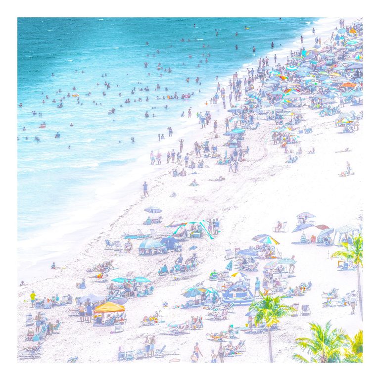 An elevated view shows swimmers in turquoise water beside a crowded pale beach scattered with colorful umbrellas, lounge chairs, and palm trees.