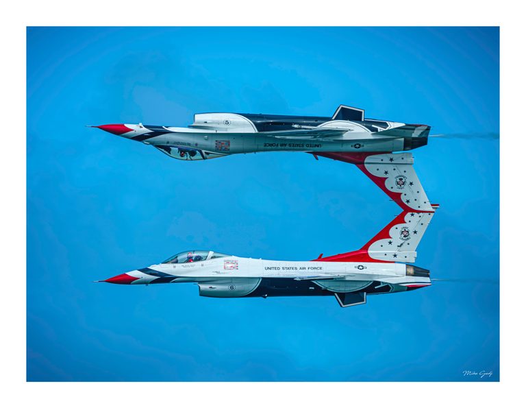 Two red, white and blue U.S. Air Force jets fly in parallel against blue sky, the upper aircraft inverted.