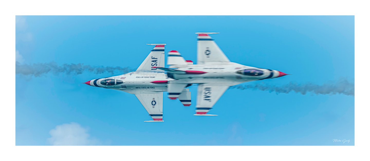 Two white jets with red and blue markings pass in opposite directions against a blue sky, trailing smoke.