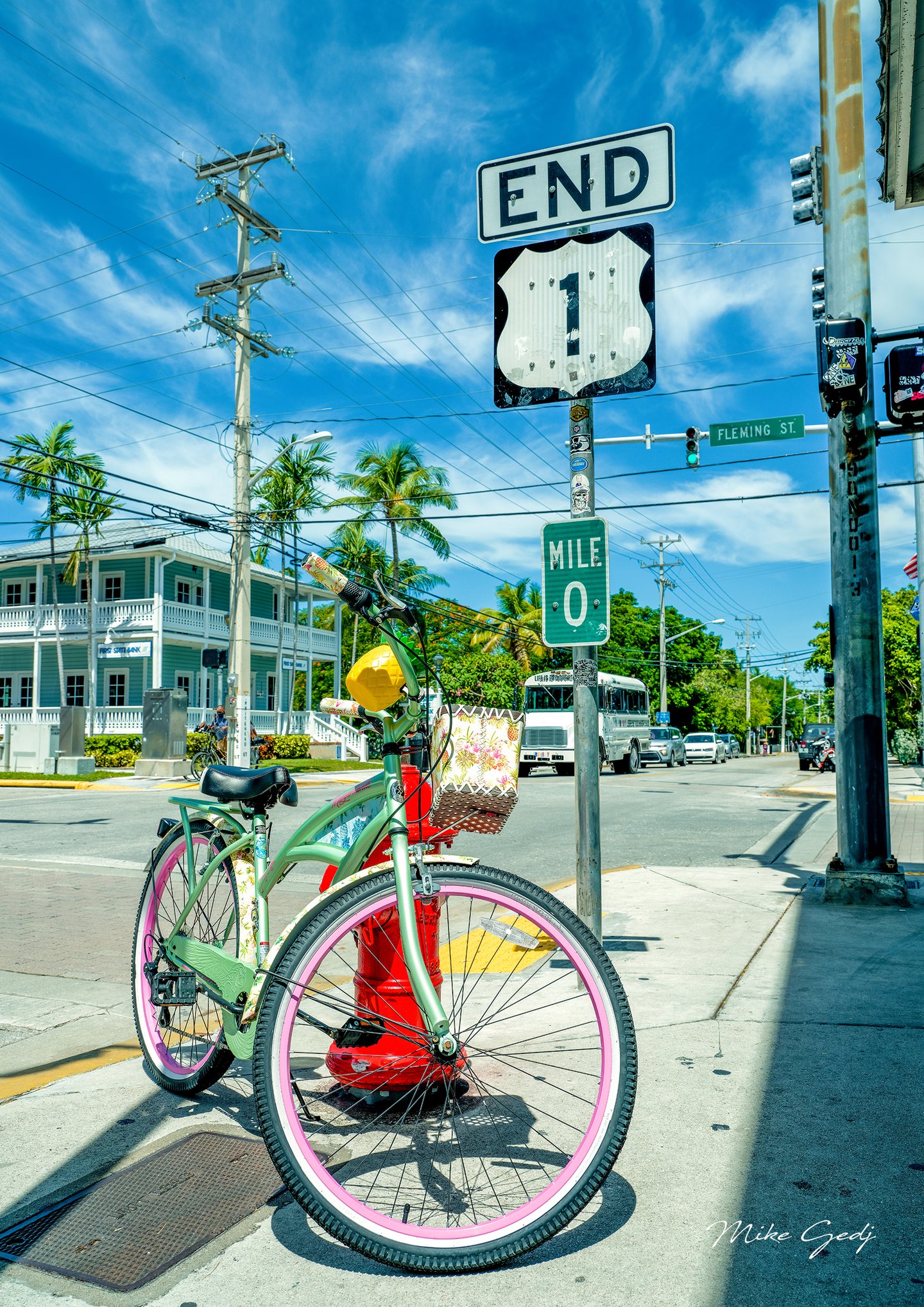 A mint-green bicycle with pink rims stands beside a red hydrant beneath Route 1 end and mile zero signs.