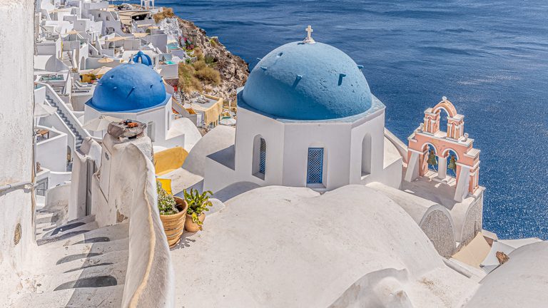 Blue-domed white churches and a peach bell tower overlook deep blue sea, with winding steps in the foreground.