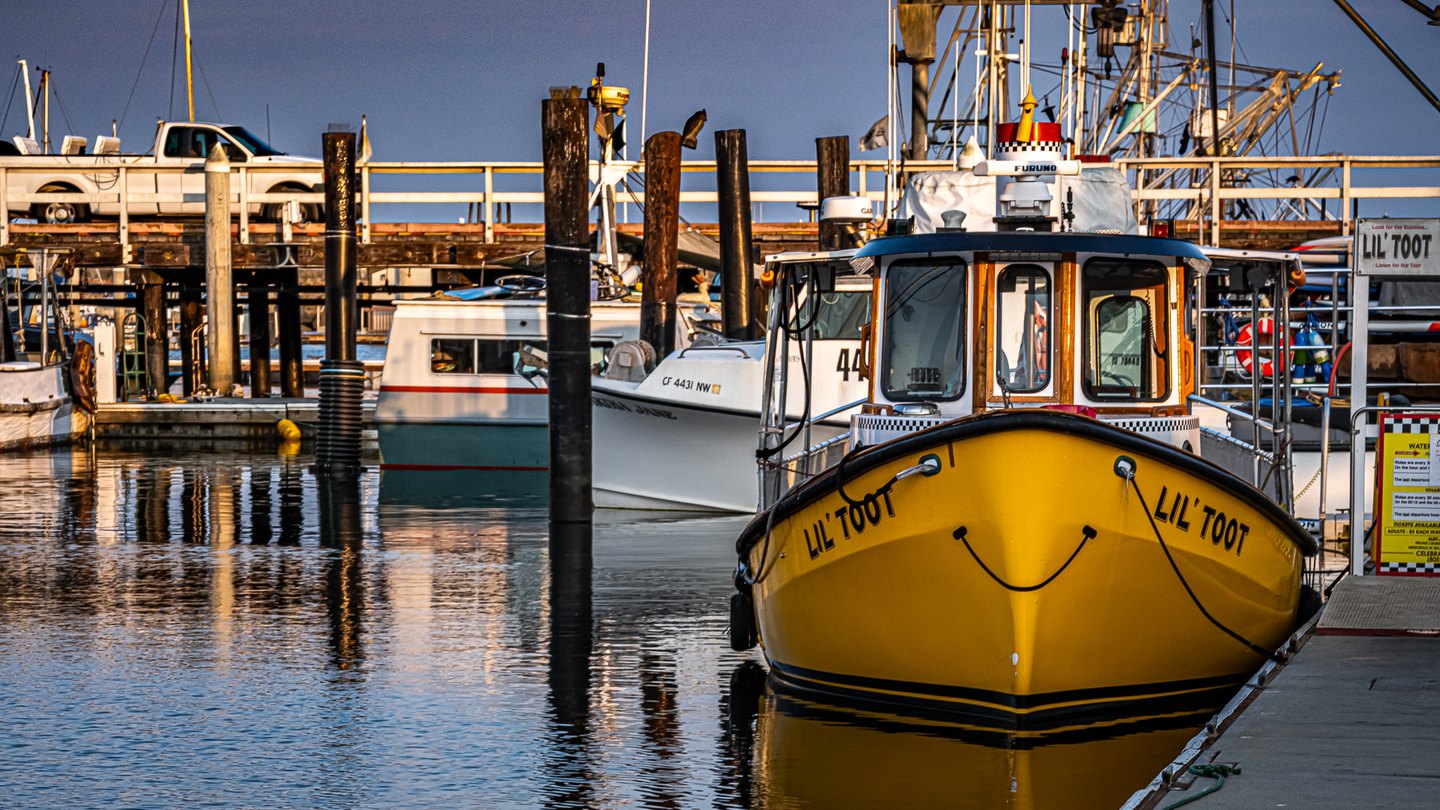 A yellow boat with a painted smile sits moored beside a dock, with other boats, pilings, and rippling reflections.