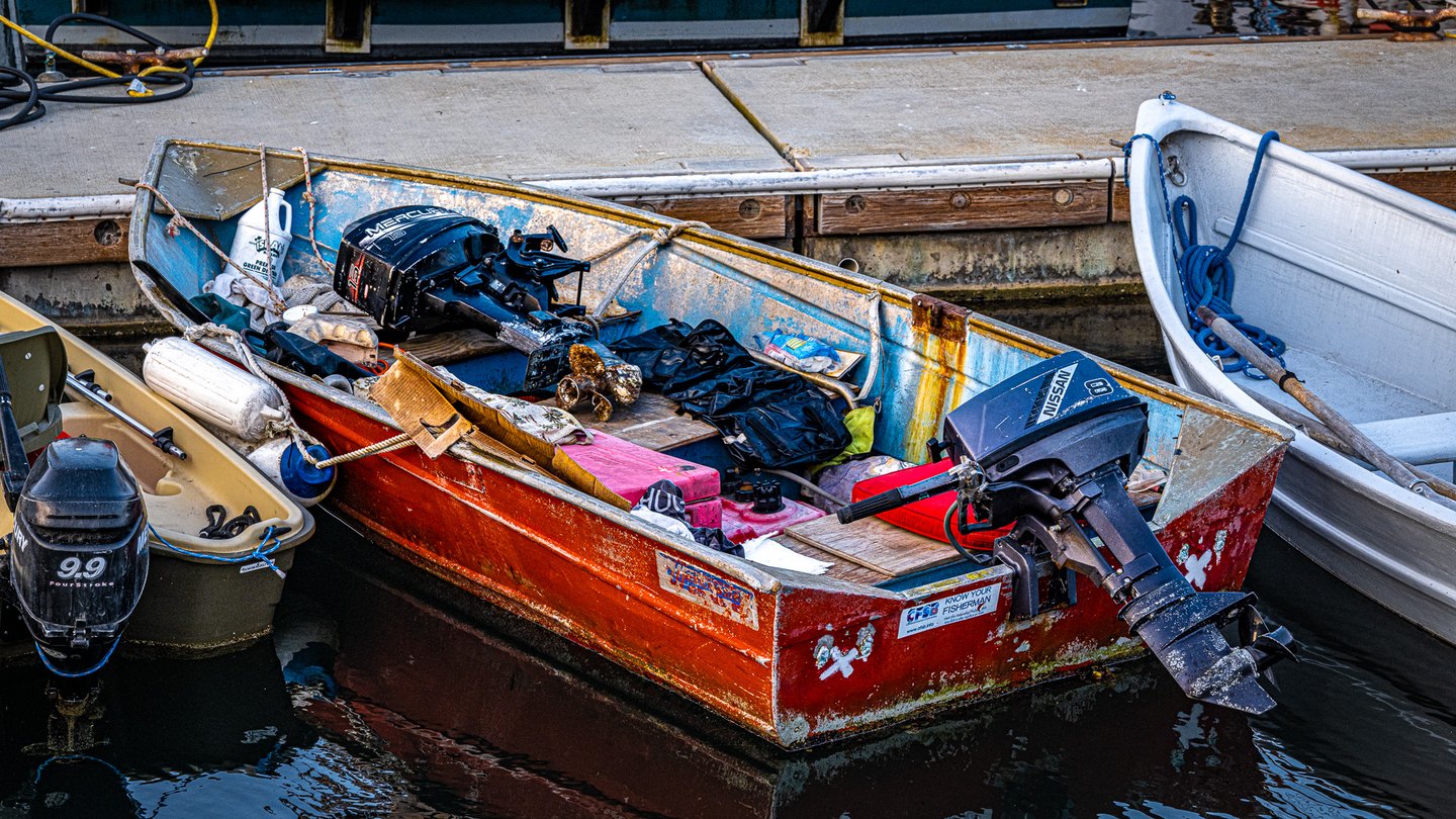 A weathered red motorboat filled with gear floats between two small boats beside a dock.