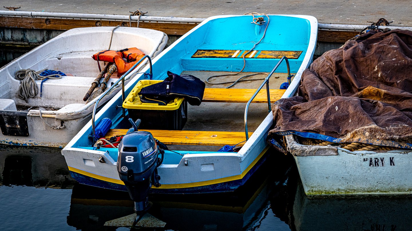 A turquoise boat with yellow benches and an outboard motor sits between two weathered boats beside a dock.