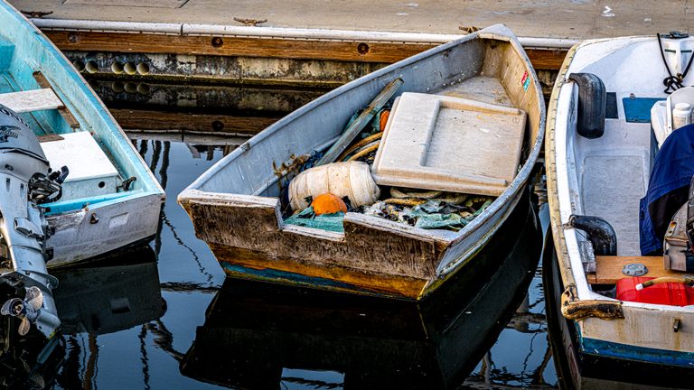 Three small boats sit beside a dock, the weathered center boat filled with ropes, floats, and fishing gear.