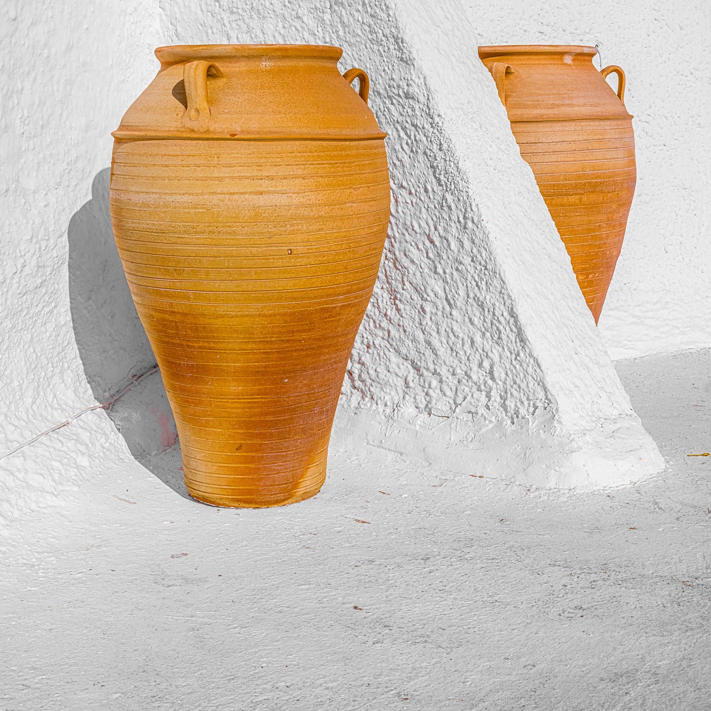 Two tall terracotta jars stand among textured white walls, one partly hidden behind a sloping partition.